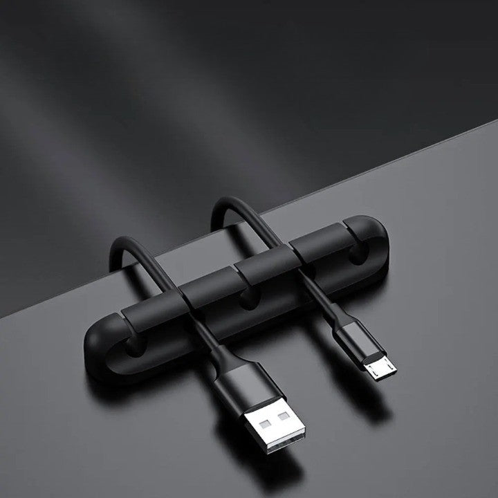 Clemă organizator cabluri din silicon negru lipită pe birou, cu cabluri USB și alimentare introduse