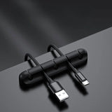 Clemă organizator cabluri din silicon negru lipită pe birou, cu cabluri USB și alimentare introduse