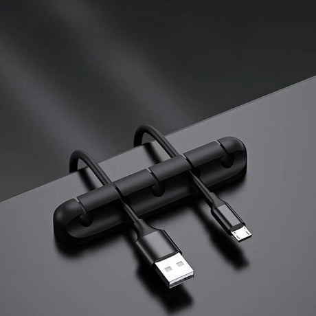 Clemă organizator cabluri din silicon negru lipită pe birou, cu cabluri USB și alimentare introduse